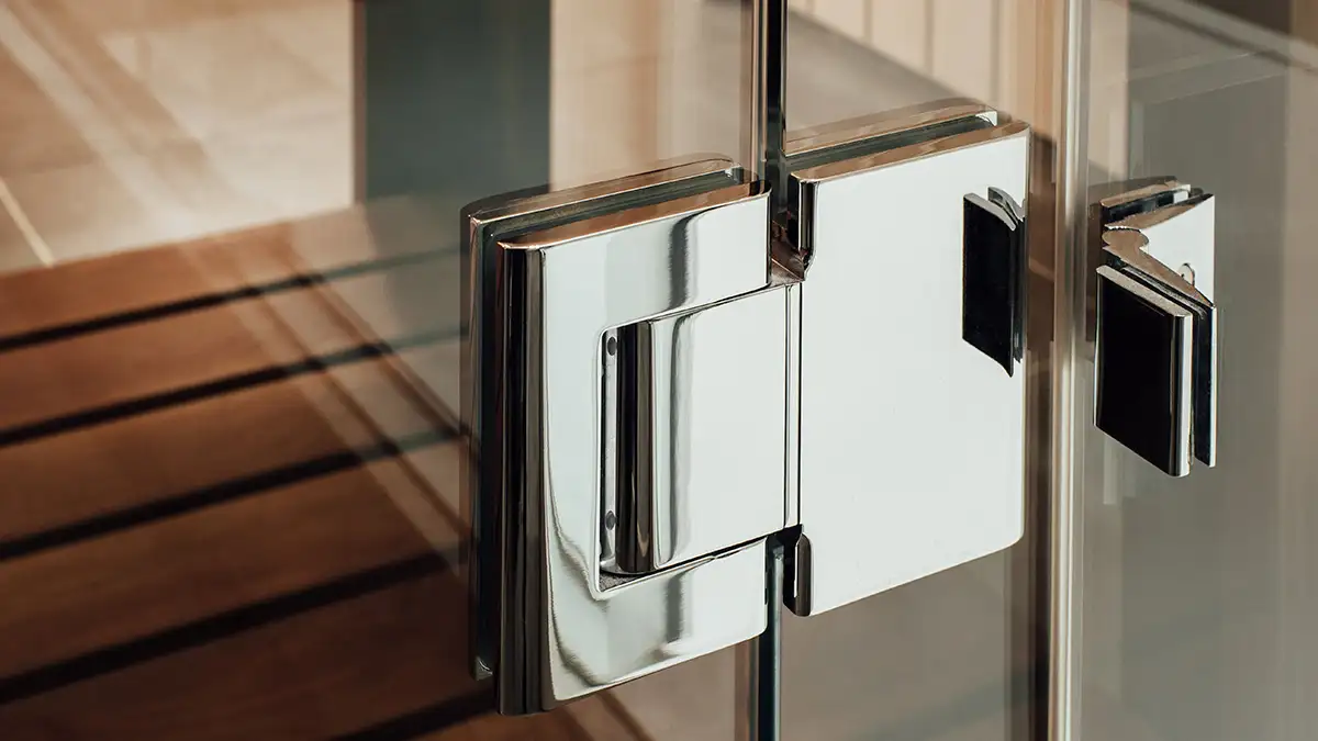 Detalle de un herraje de acero inoxidable para puerta de vidrio, reflejando la tendencia minimalista.